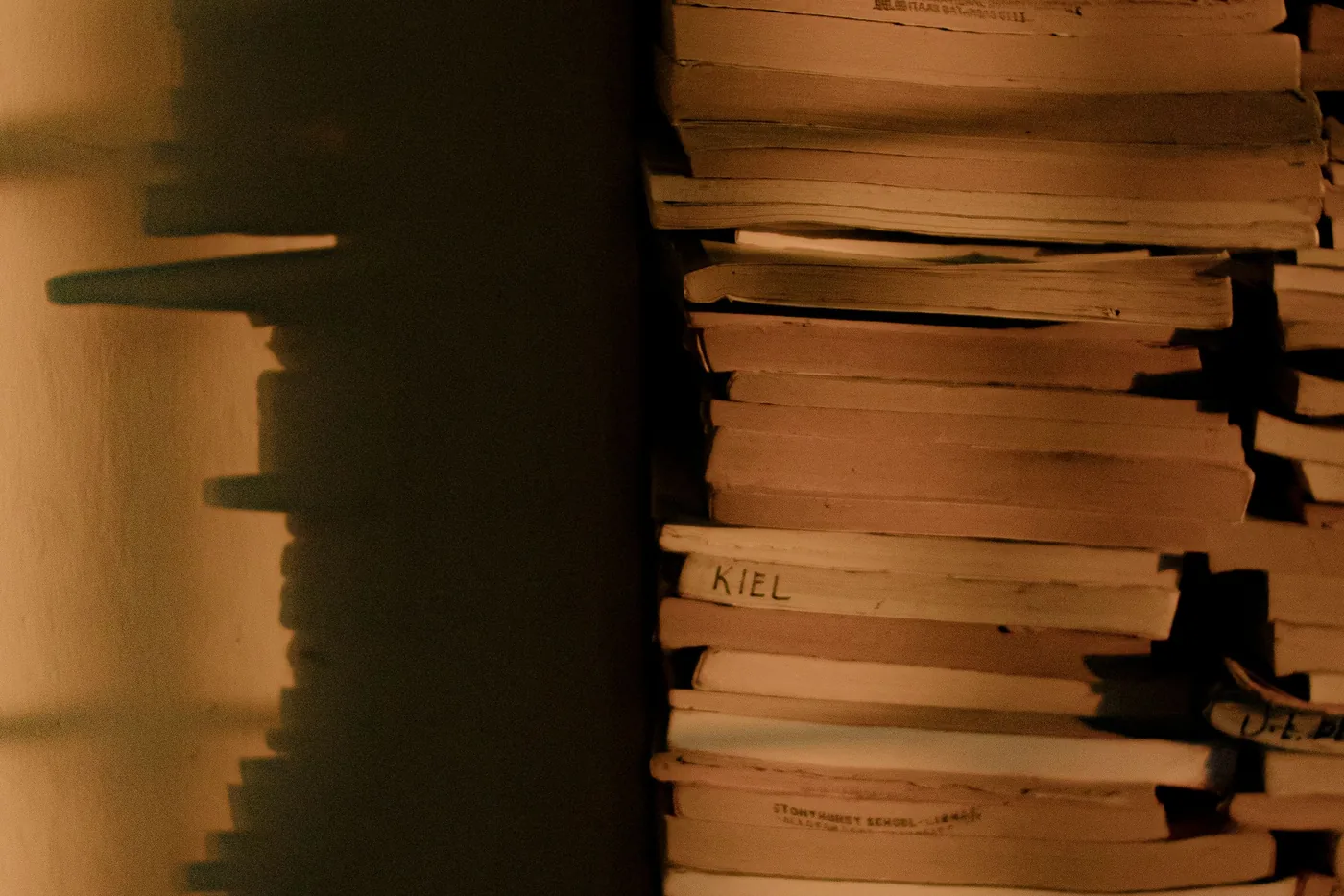 Hoher Stapel Papierbögen an einer Wand, warmes Streiflicht wirft den Schatten des Stapels daneben