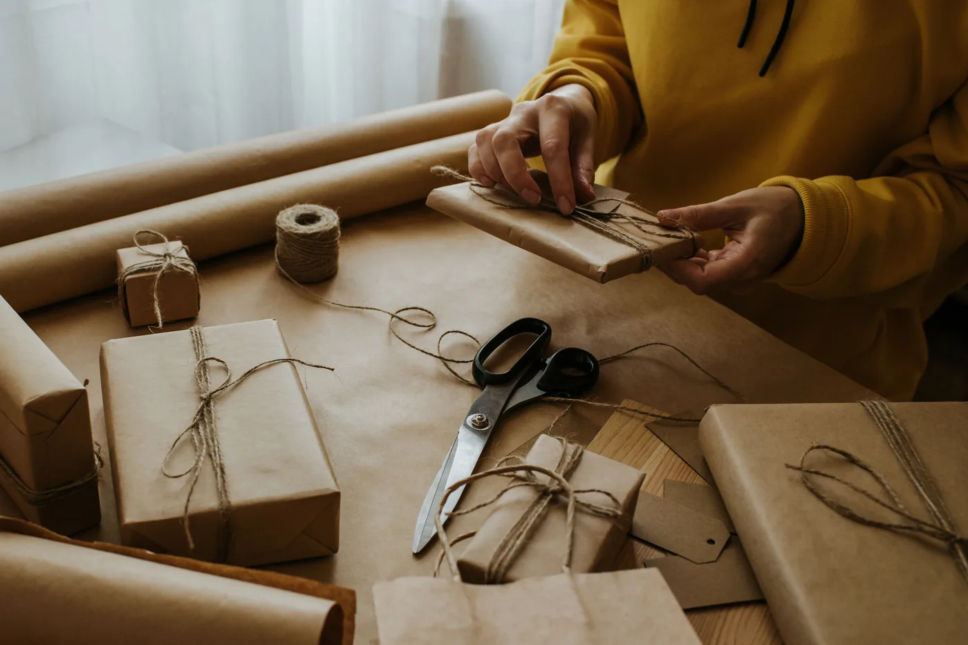 Hände verschnüren ein in Kraftpapier eingeschlagenes Paket mit Naturschnur