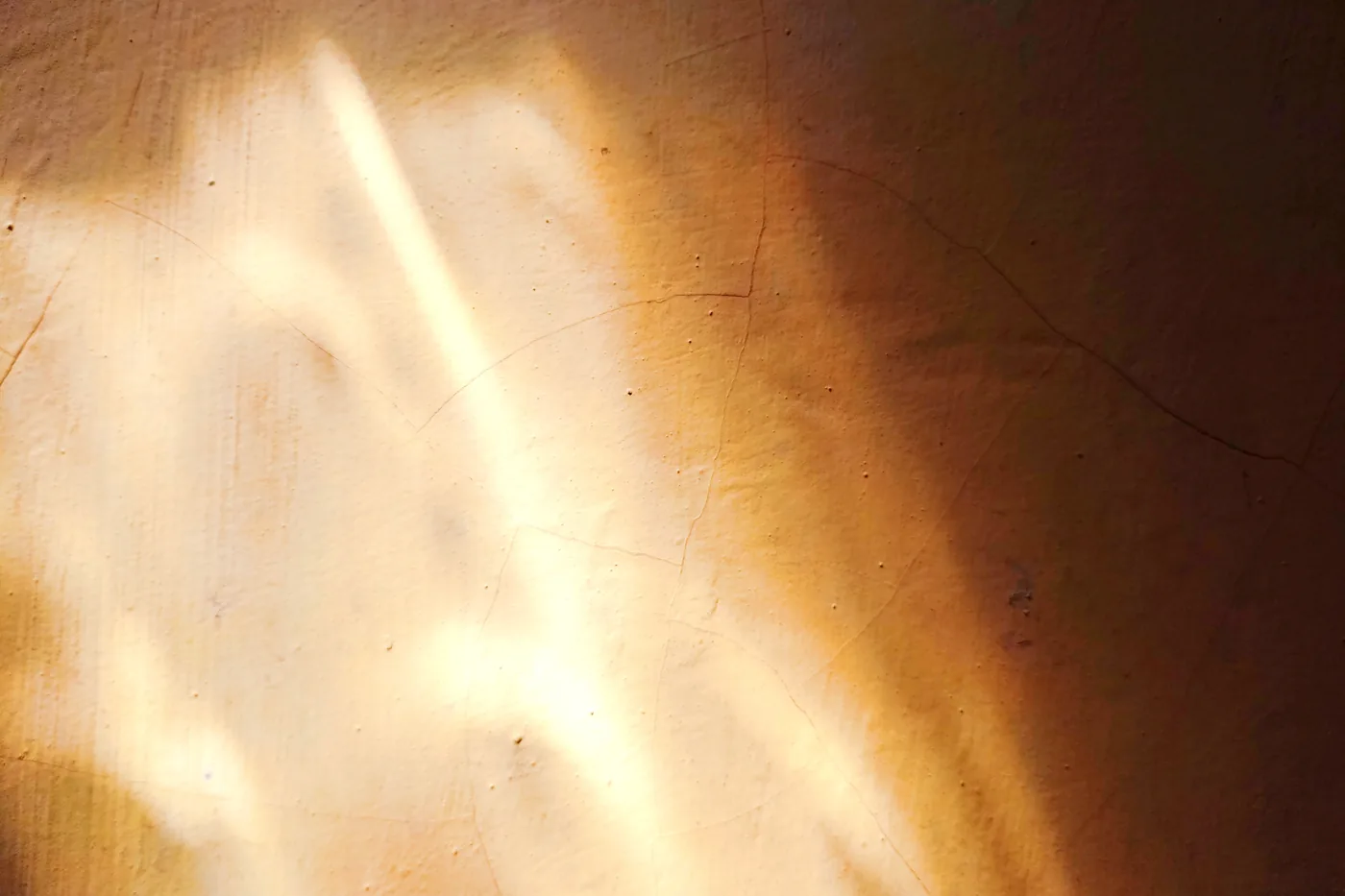 Sonnenlicht fällt durch eine Öffnung in Lichtbahnen auf eine warme Putzwand