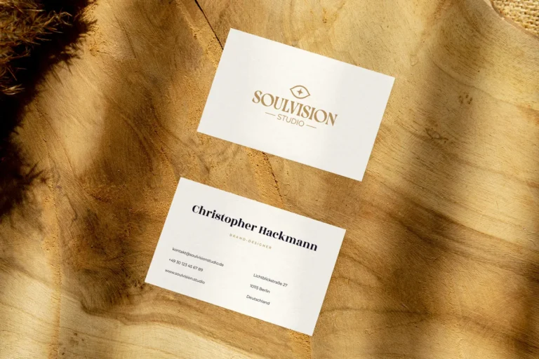 Zwei Visitenkarten von SoulVision Studio auf warmem Holz: vorne das Logo mit Auge und Schriftzug, hinten Name und Kontaktangaben