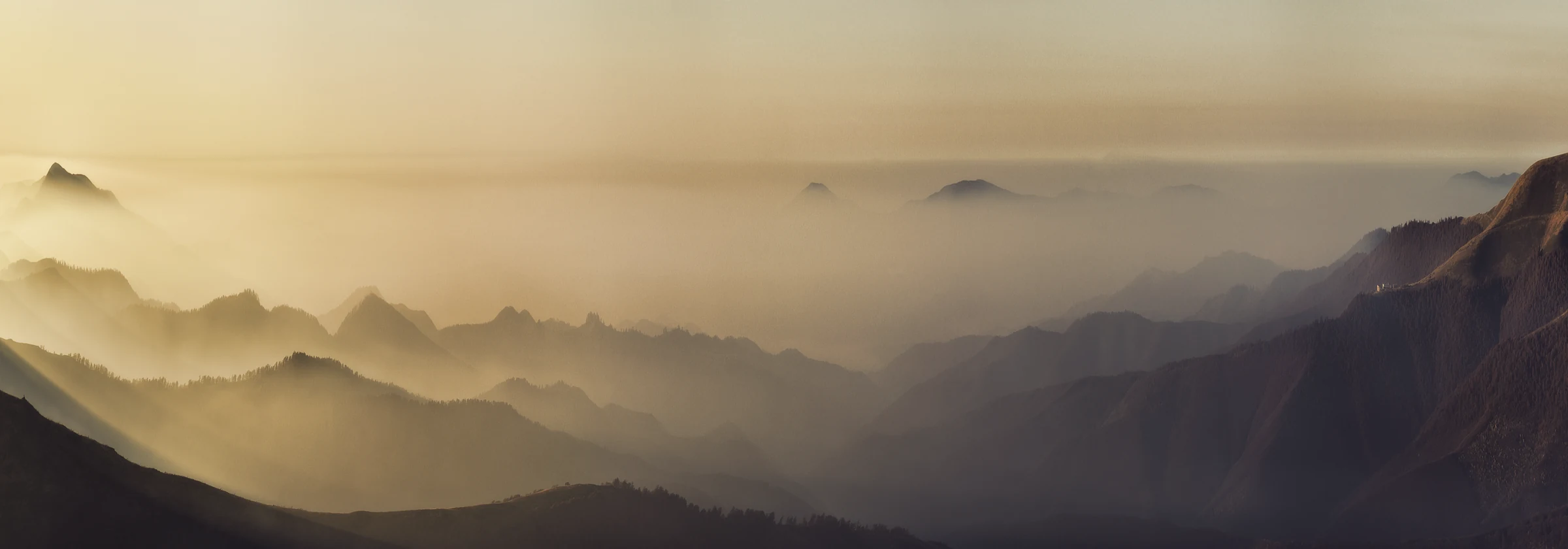 Mehrere hintereinanderliegende Bergketten im warmen Abendlicht, Sonnenstrahlen fallen schr&auml;g &uuml;ber die H&auml;nge, der Dunst wird nach hinten heller.