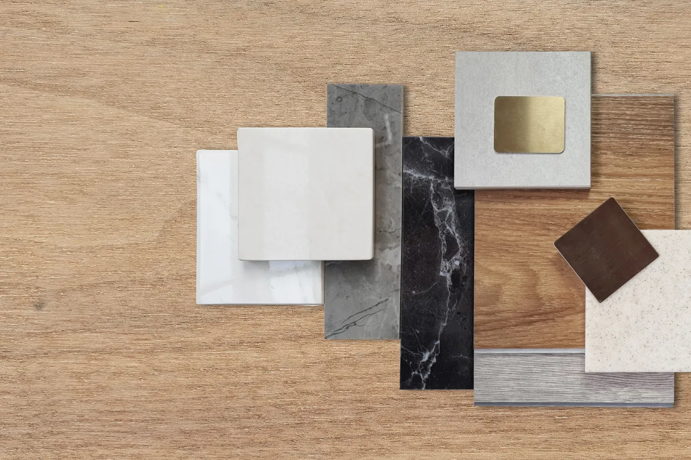 Materialmuster nebeneinander auf einem Holztisch: Marmor, Holzdielen, Keramik und gebuerstetes Messing